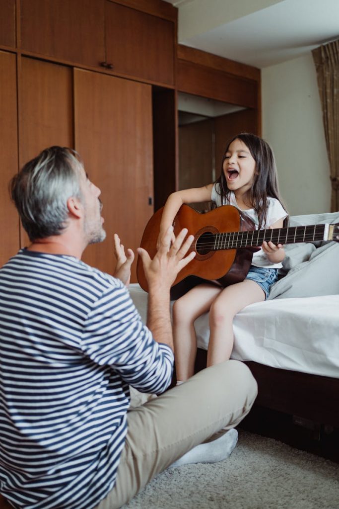 Father and daughter bonding through music, playing guitar together at home.